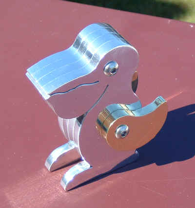 Silver metal pelican-shaped object on reddish-brown surface.