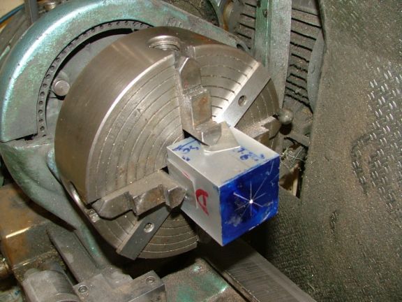 A metalworking lathe chuck with a blue and white square calibration tool attached.