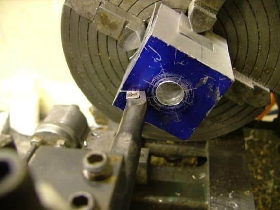 Blue metal component with central silver ring attached to large machinery, precision work setup.