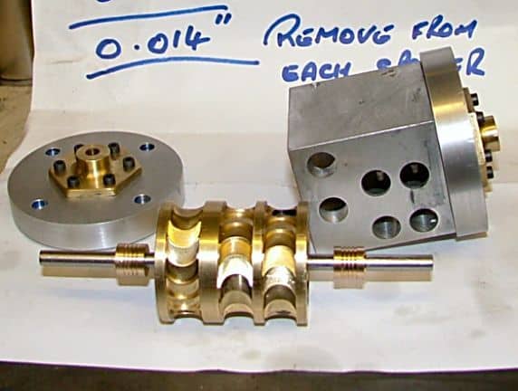 Metal parts on white paper with handwritten notes in a workshop setting.