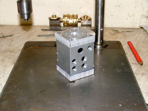 Metal block with cylindrical top, rectangular bottom, and four holes on one side.