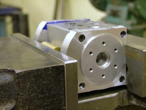 Silver metal block with cylindrical hole and multiple holes on top.