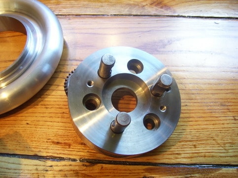 A shiny metallic 5C chuck with three holes and central star-patterned hole on a light-colored wooden surface.