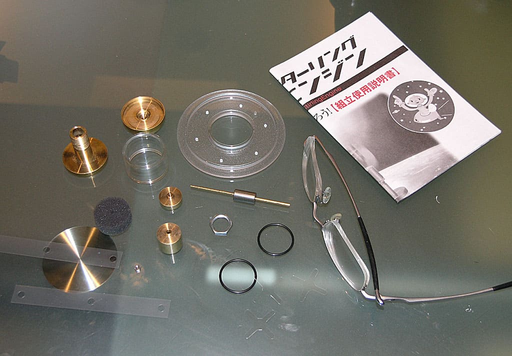Metal components, tools, and accessories on a surface with safety glasses nearby.