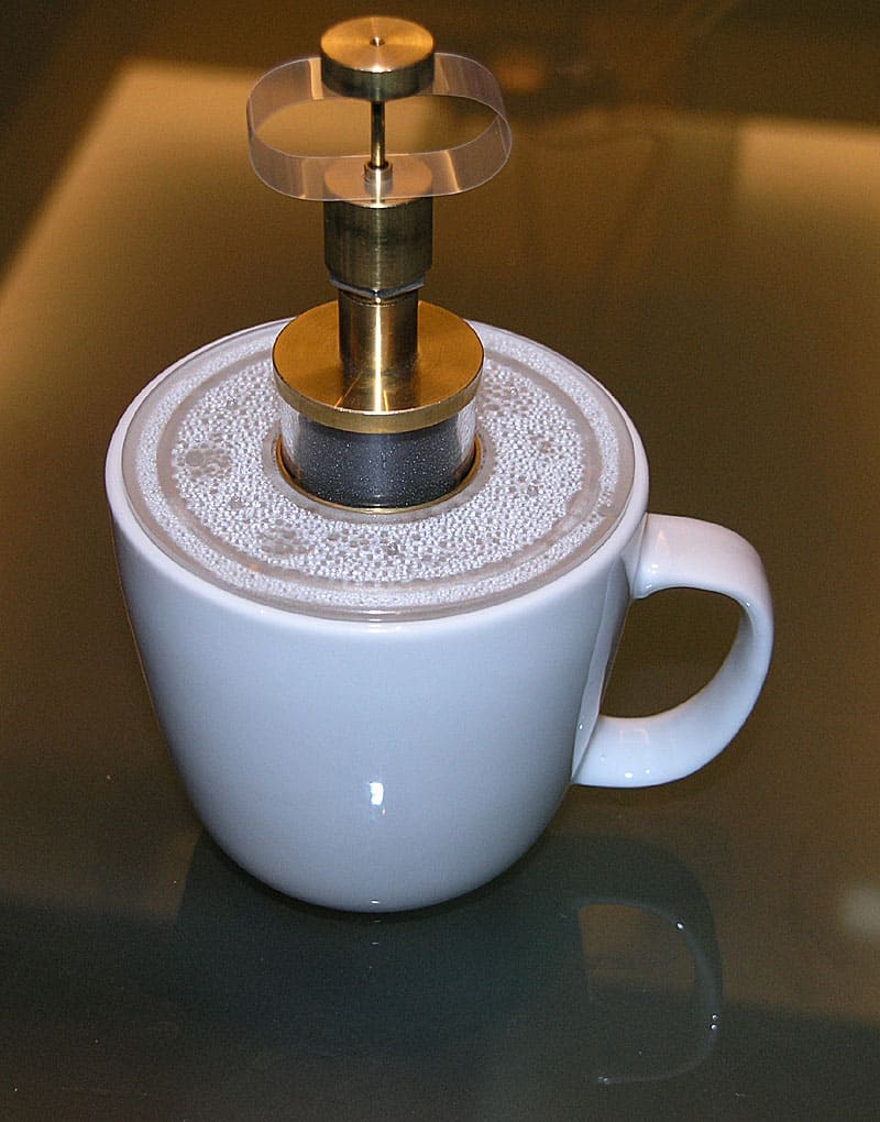 Metal device with metal cylindrical stem on top of white coffee mug.