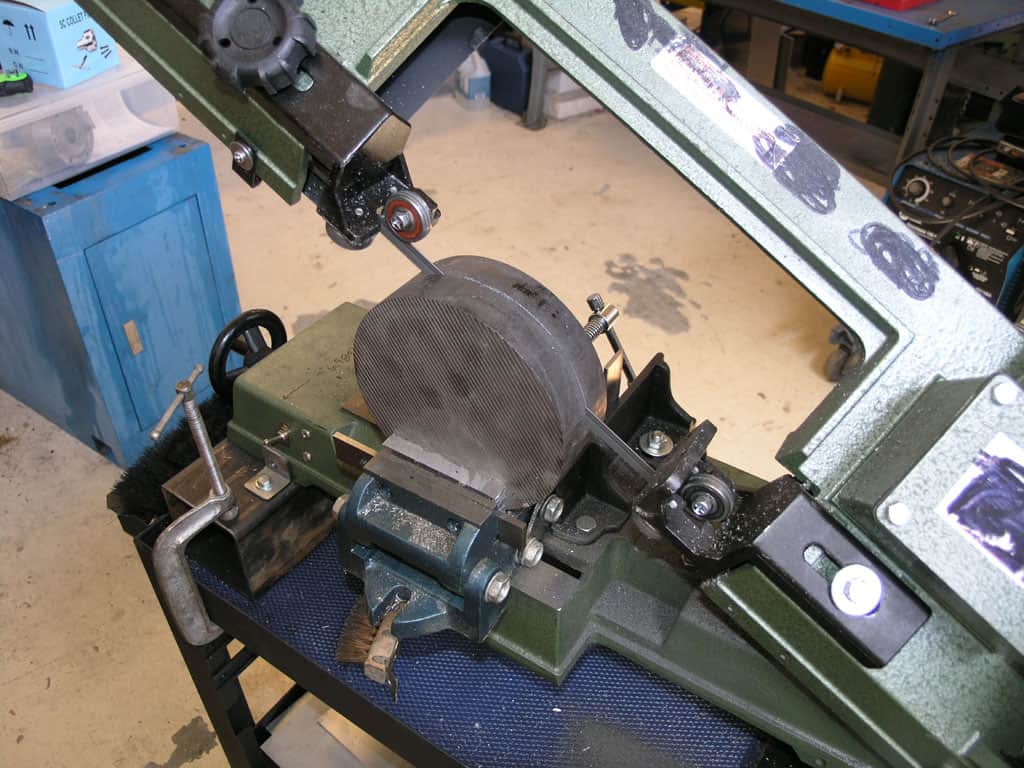 Large green metal cutting machine in a workshop setting with visible wear and tear, surrounded by other machinery and tools.