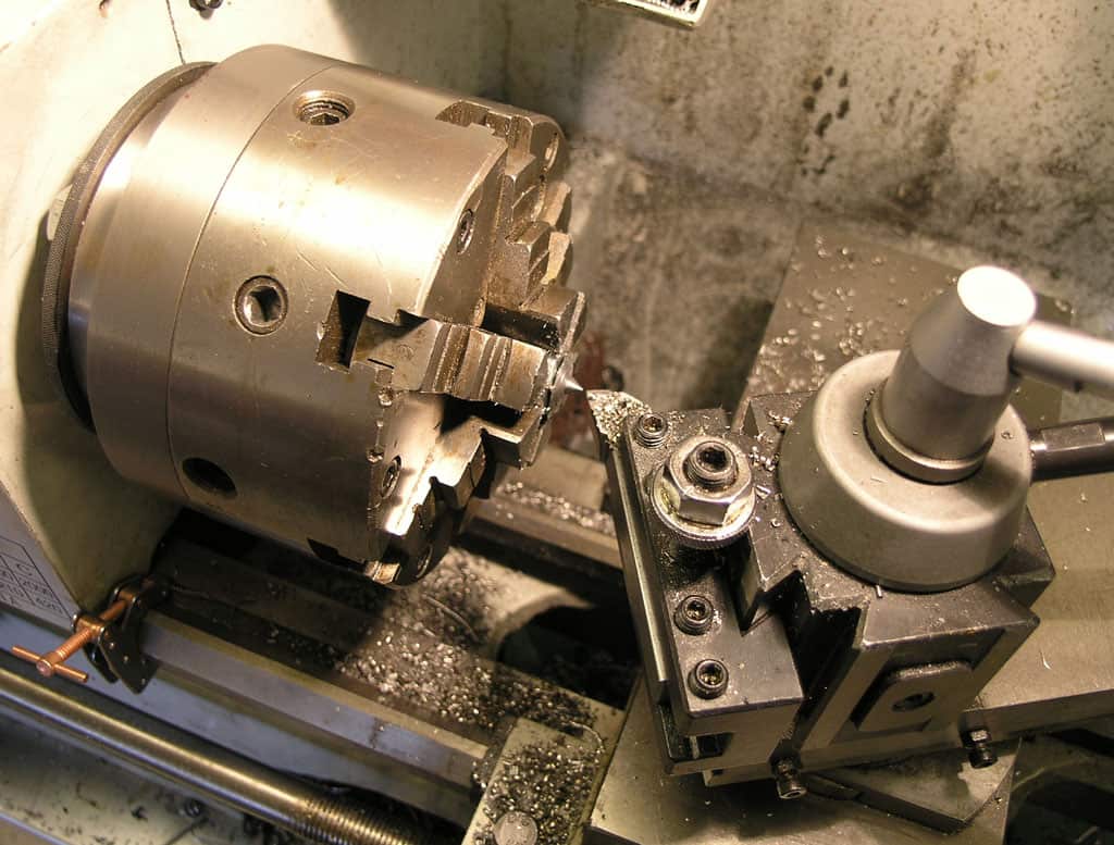 Metal lathe tool with cylindrical head and multiple holes, along with a small round attachment.