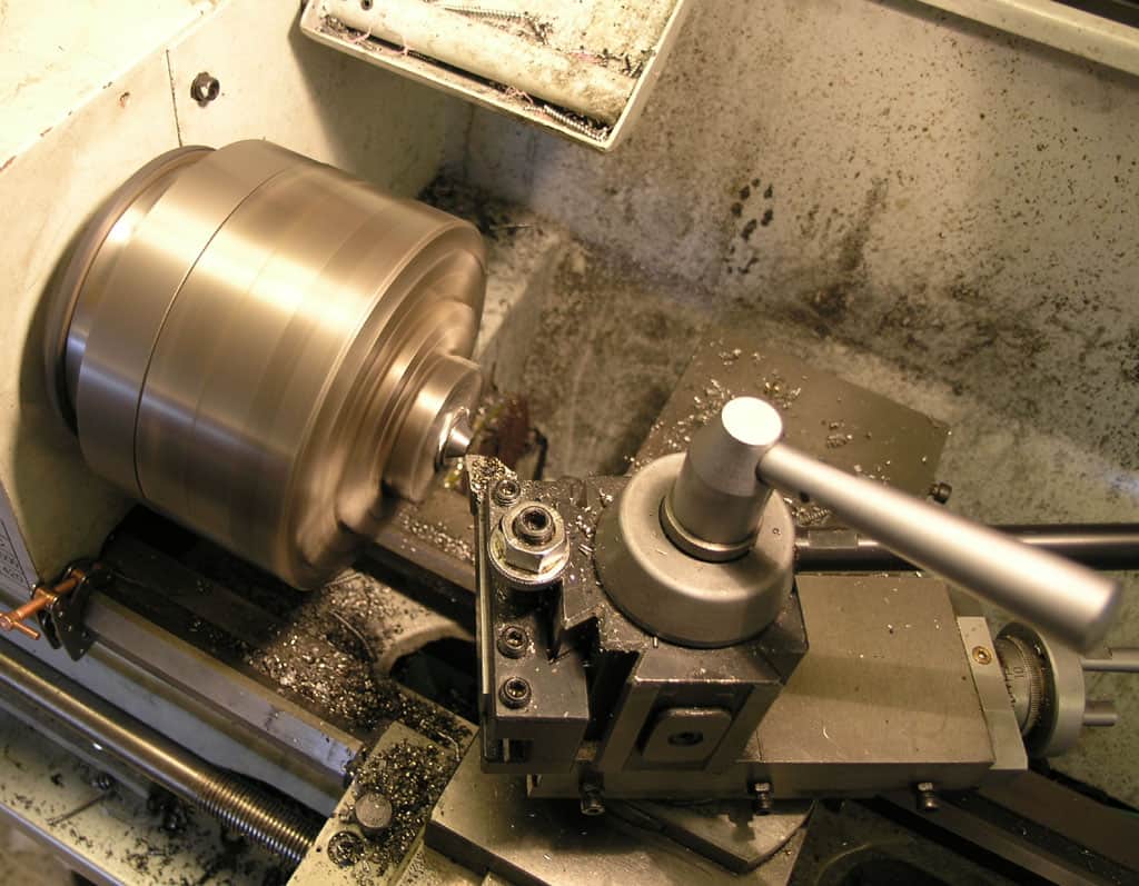 Metalworking lathe in industrial setting with rotating spindle, chuck, and surrounding metal shavings.