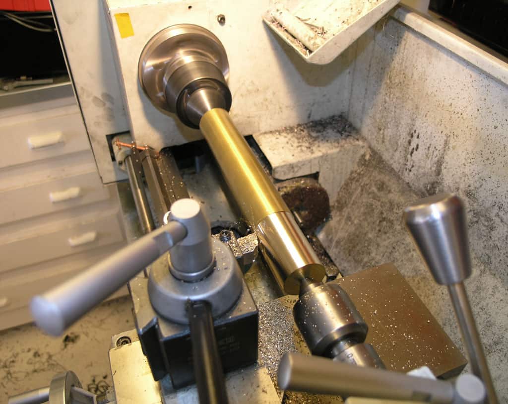 A lathe machine on a table in an industrial setting with components, workpiece, drawers, and other machinery.