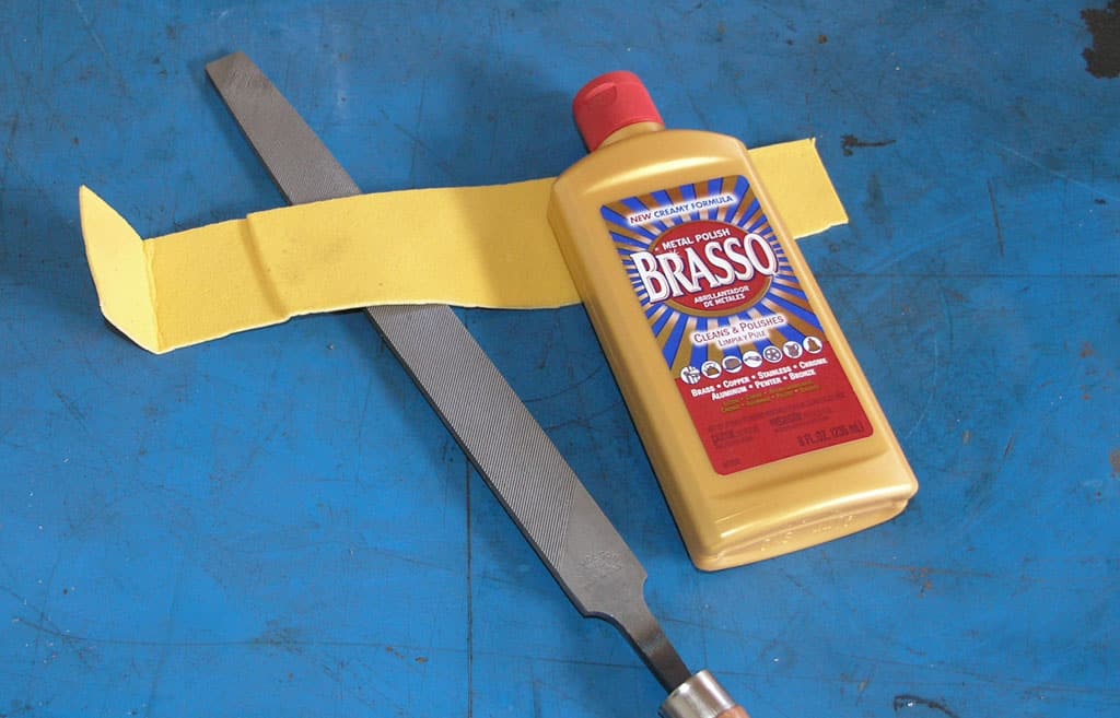 Brasso metal polish with yellow label and blue accents sitting on a workbench.