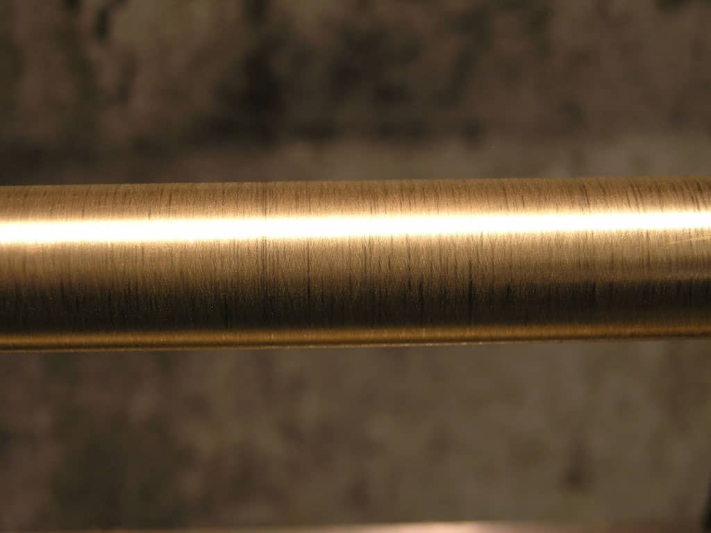 A close-up image of a shiny metallic surface with a brushed finish, possibly made of brass or bronze, featuring a warm golden color and subtle sheen.