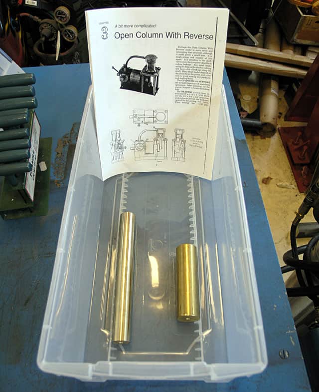 Plastic container with two brass tubes on a blue workbench containing a printed instruction manual.