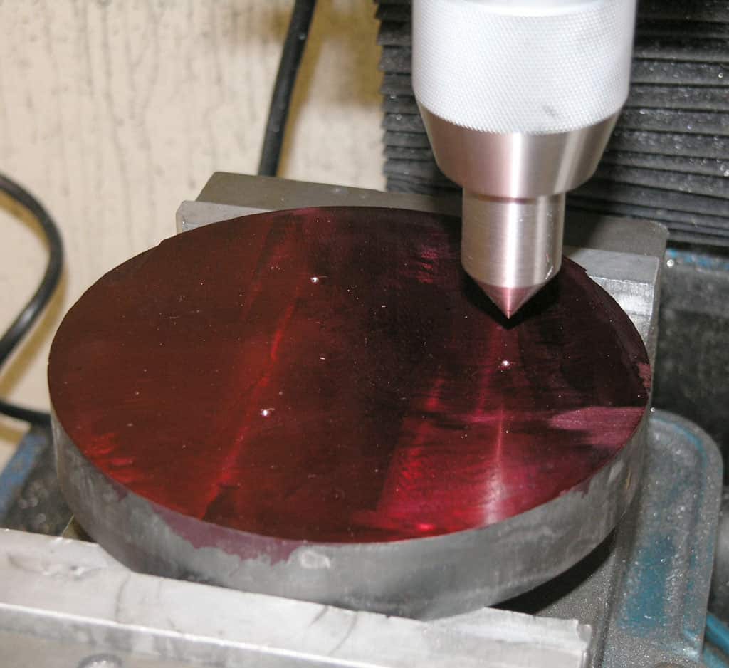 Ruby-tipped diamond cutter on a metalworking machine, showcasing red stylus with pointed tip over a circular metal object.