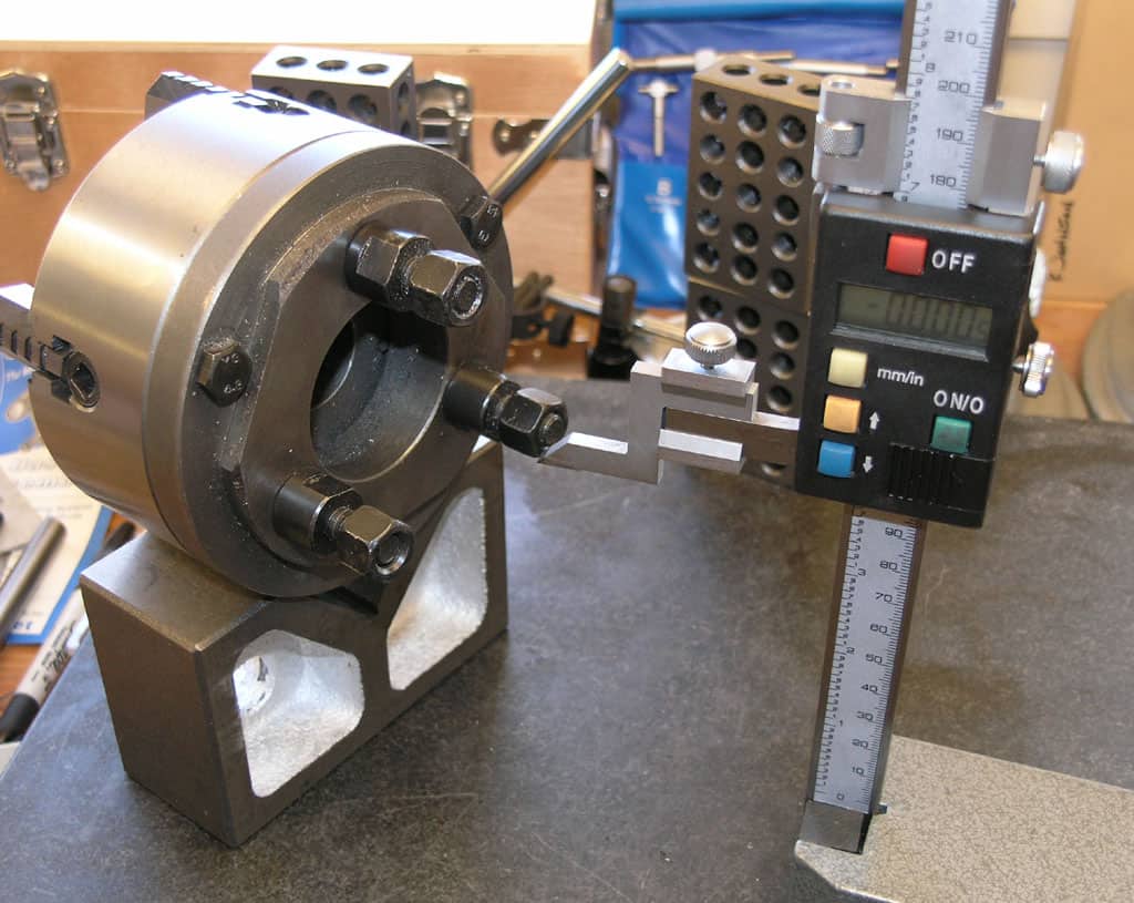 Digital caliper with black body, silver blade, and LCD screen on a black table surrounded by various tools and equipment.