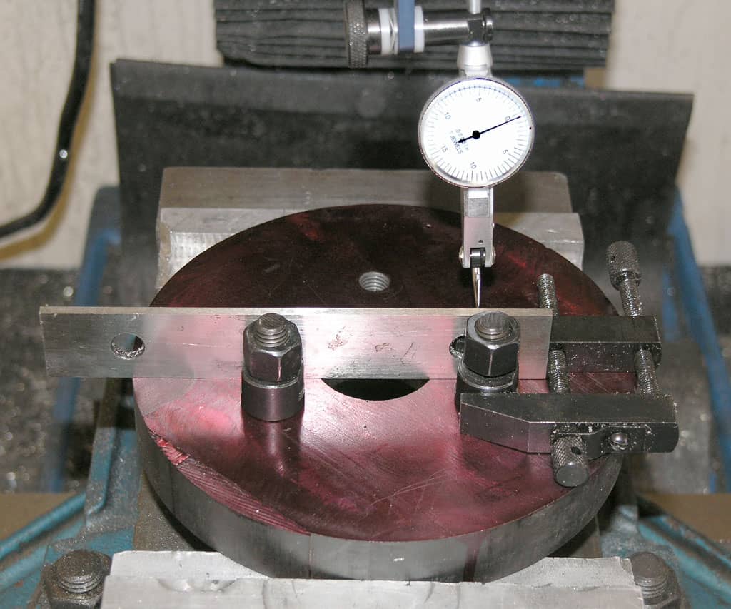 Precision measurement tool with circular base, central hole, two parallel arms, metal rods, and attached dial indicator.