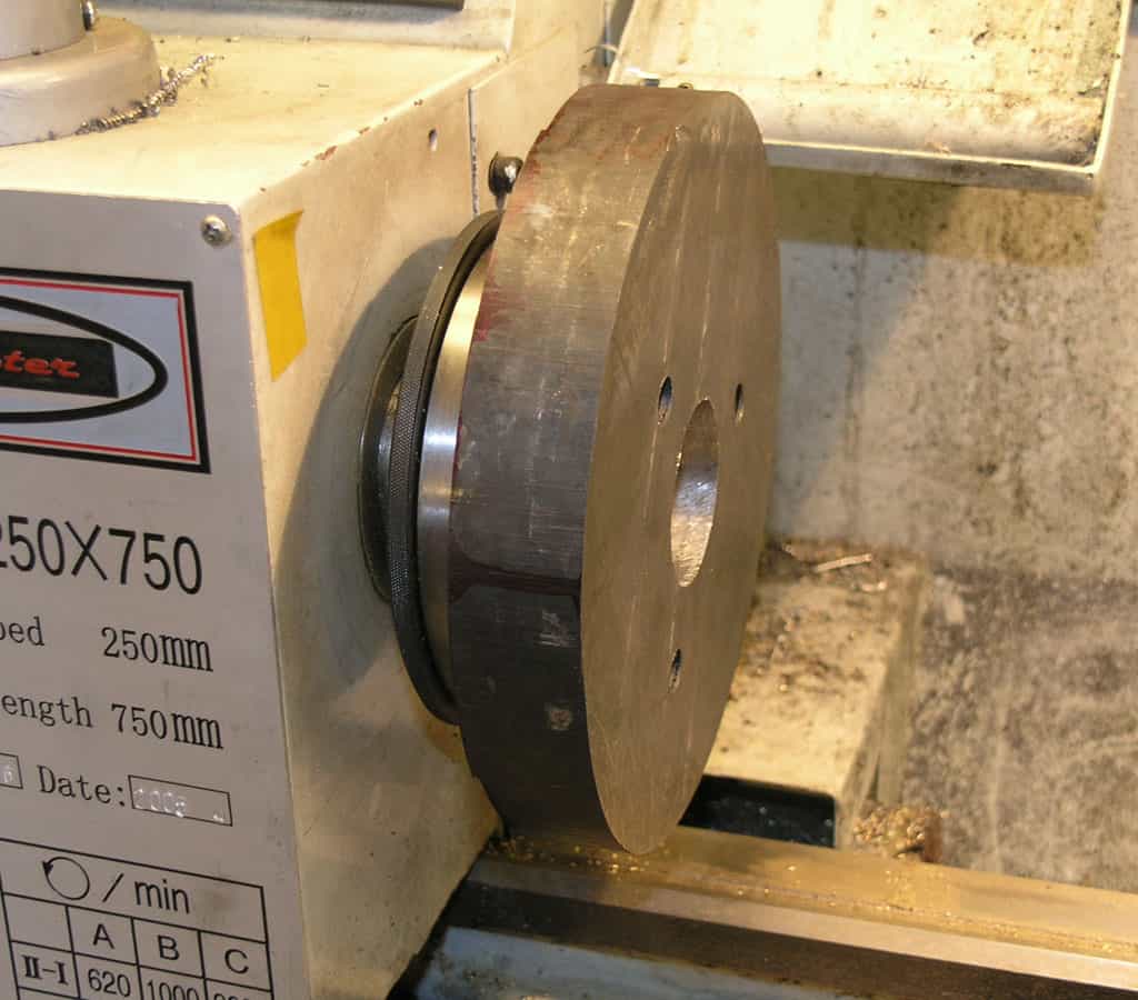 Metal wheel on a machine with red and black labeling and a dirty workshop background.