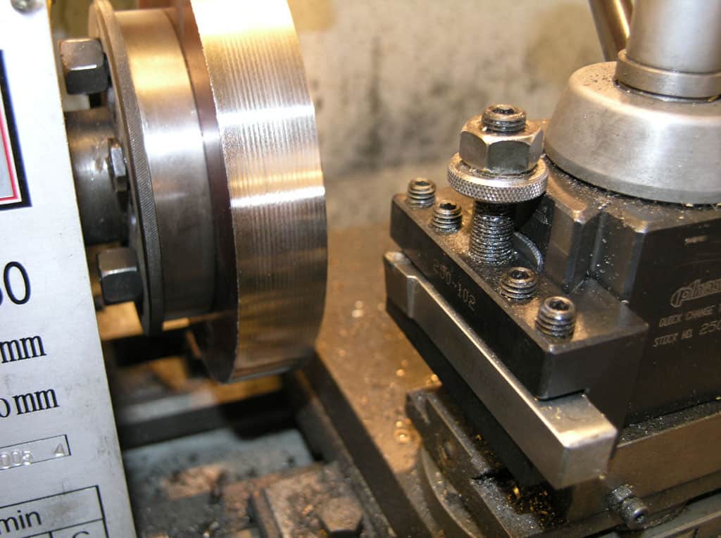 Metal lathe with tool rest and chuck holding a cylindrical workpiece.