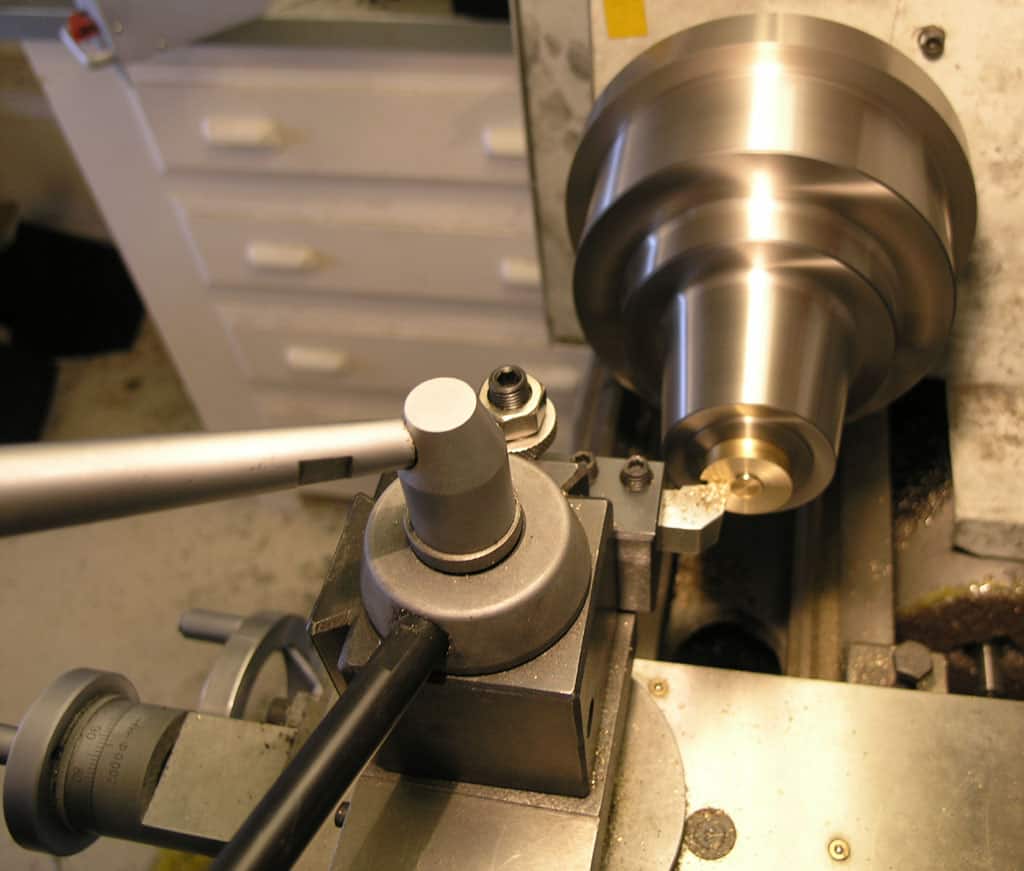 A lathe machine with spindle, metal rod, tool holder, and cord.