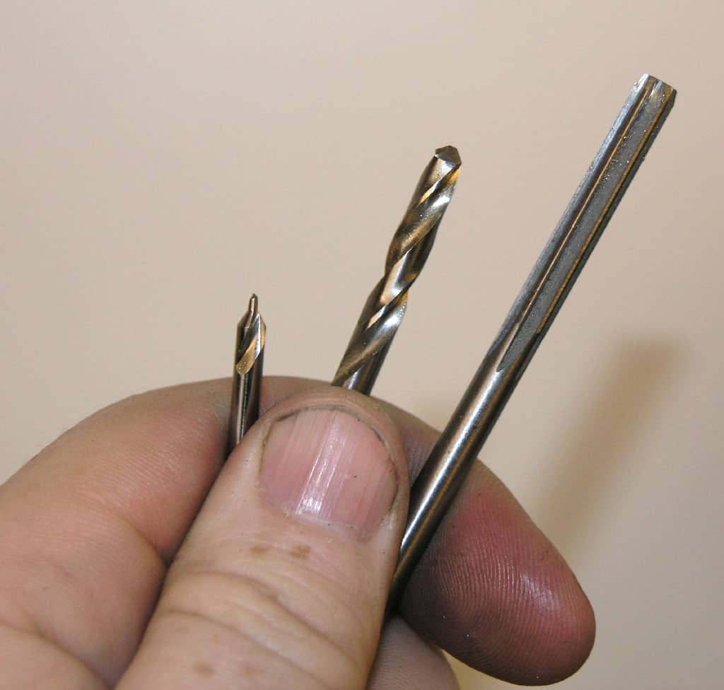 Hand holding three silver metal drill bits against an off-white background.
