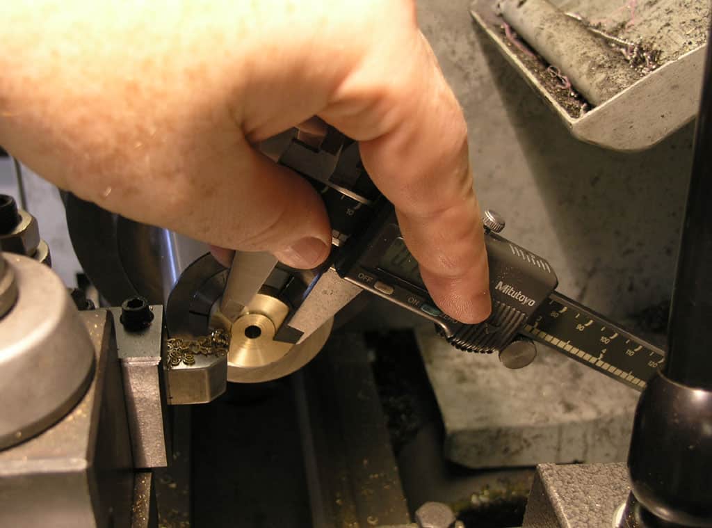 A person holding an adjustable digital caliper with "Mitutoyo" branding and pointing to a measurement display.