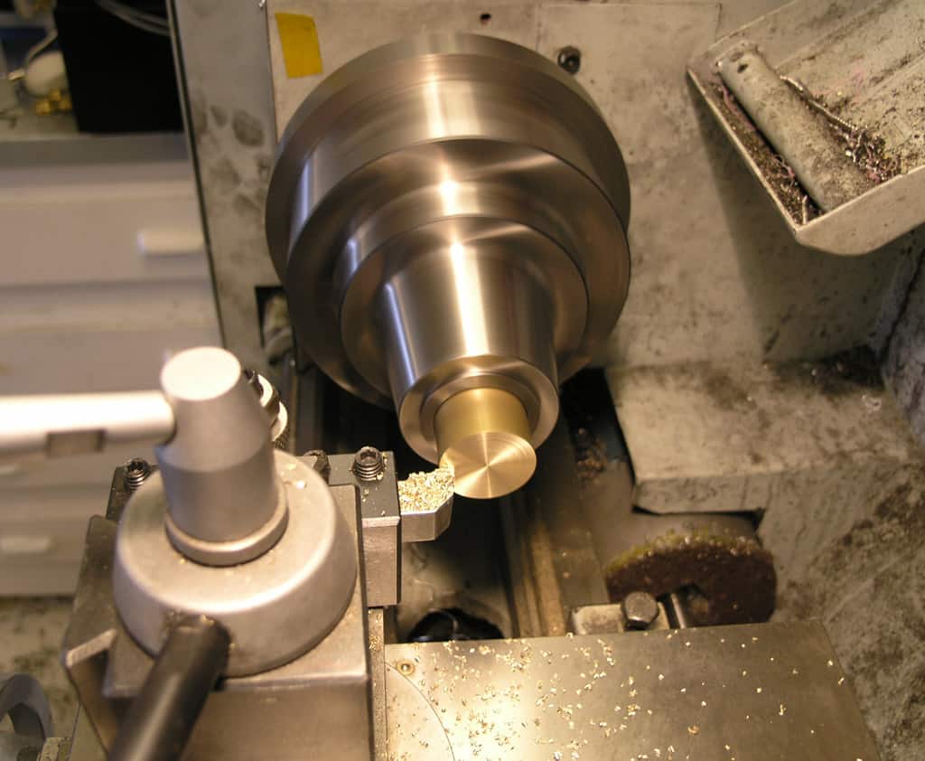 Metal lathe with large brass piece being machined. Stainless steel lathe with brass workpiece.