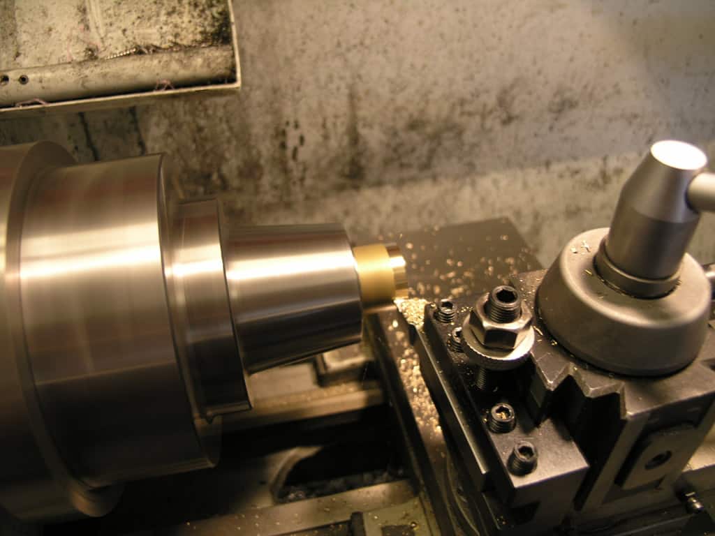A metallic lathe tool in an industrial setting, cylindrical shape with small circular hole.