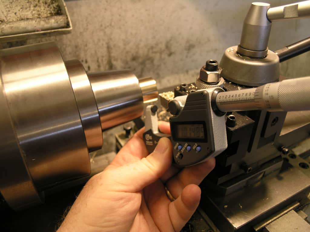 Digital micrometer being held by a hand against a large metal object.