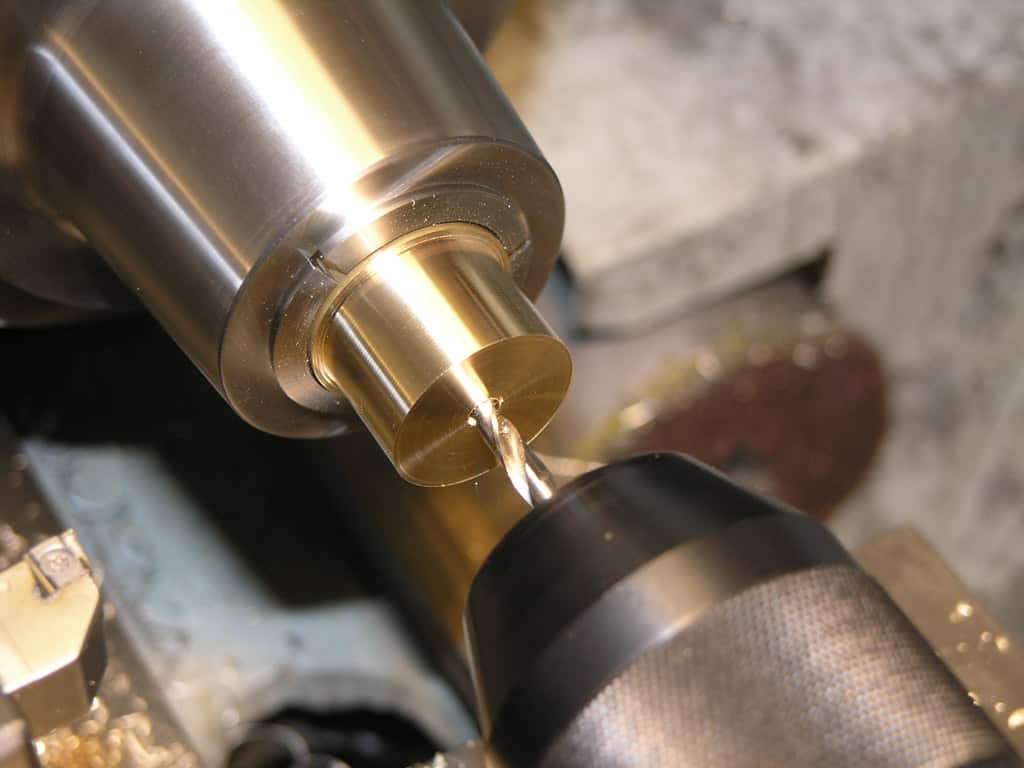 A close-up photograph of a drill bit in a lathe, highlighting machine shop equipment and metal fabrication craftsmanship.
