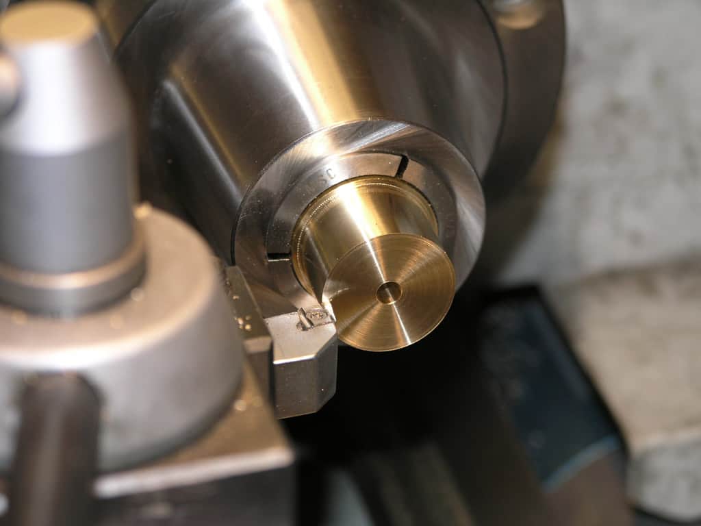 Close-up view of a lathe's stainless steel spindle with brass chuck gripping a cylindrical workpiece.
