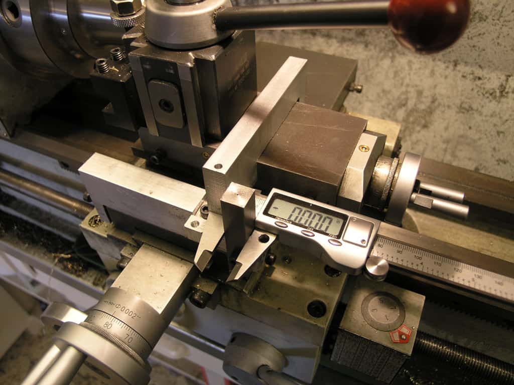 A metalworking lathe with a digital caliper measuring a workpiece.