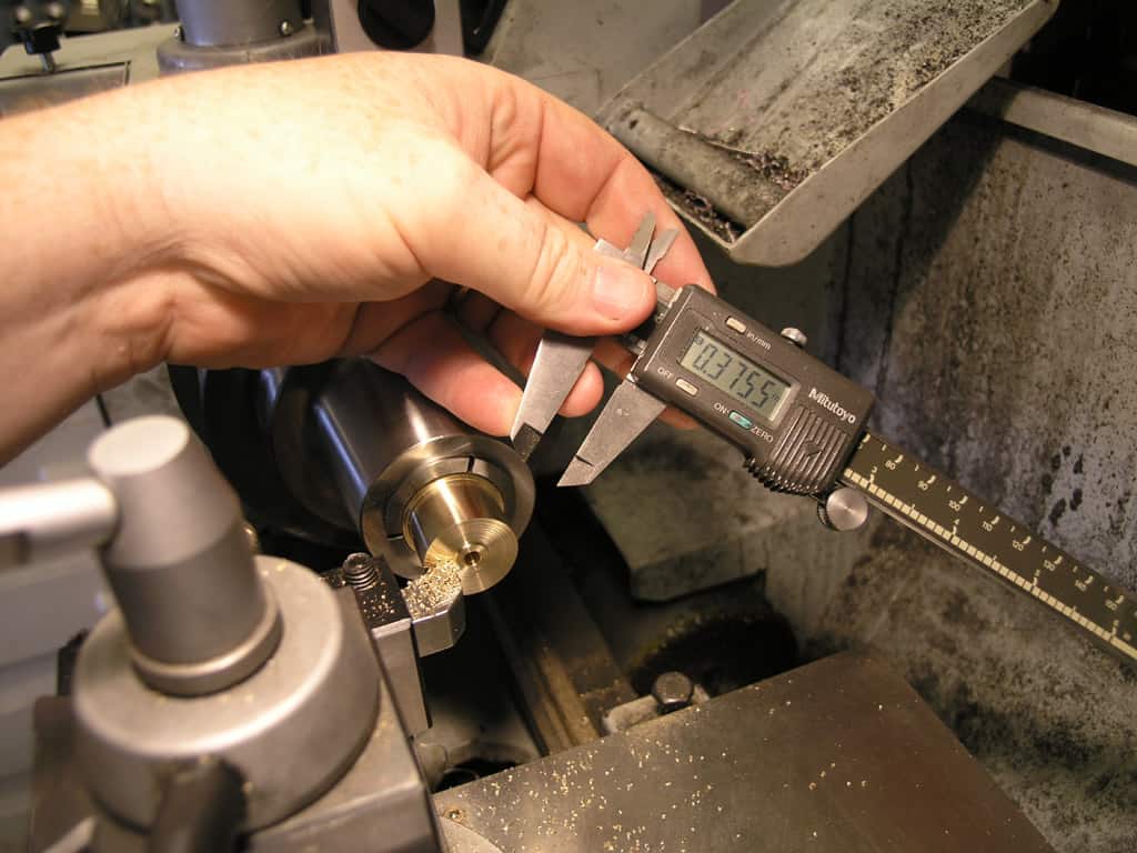 A person holding a digital caliper measuring a metallic object.