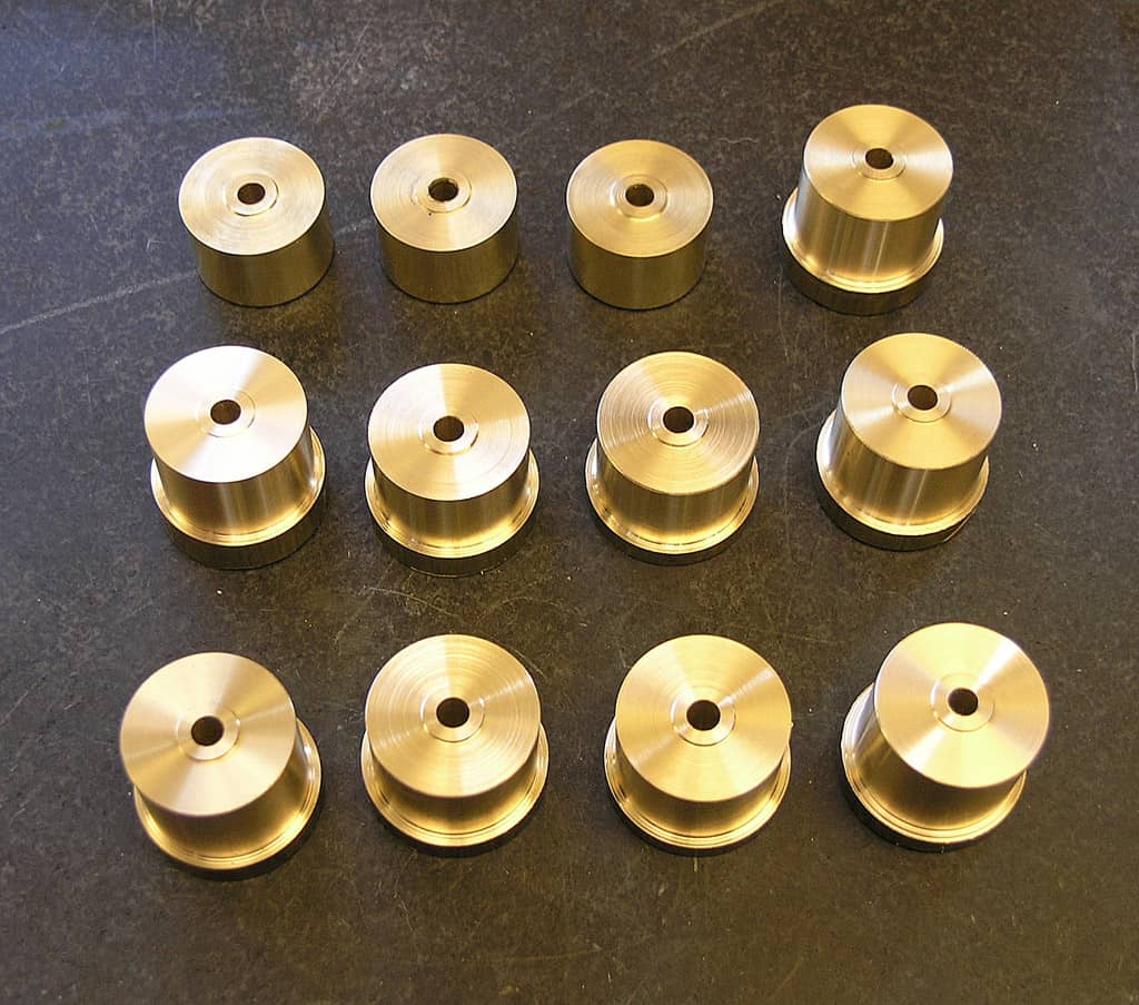 Cylindrical brass parts with central hole and smooth surface arranged in a grid on a dark gray background.