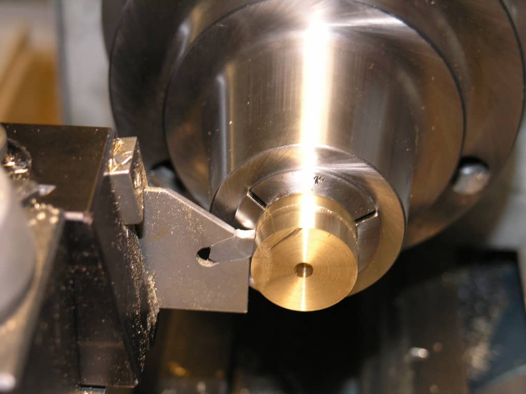 Metal component on lathe tool post in workshop setting.