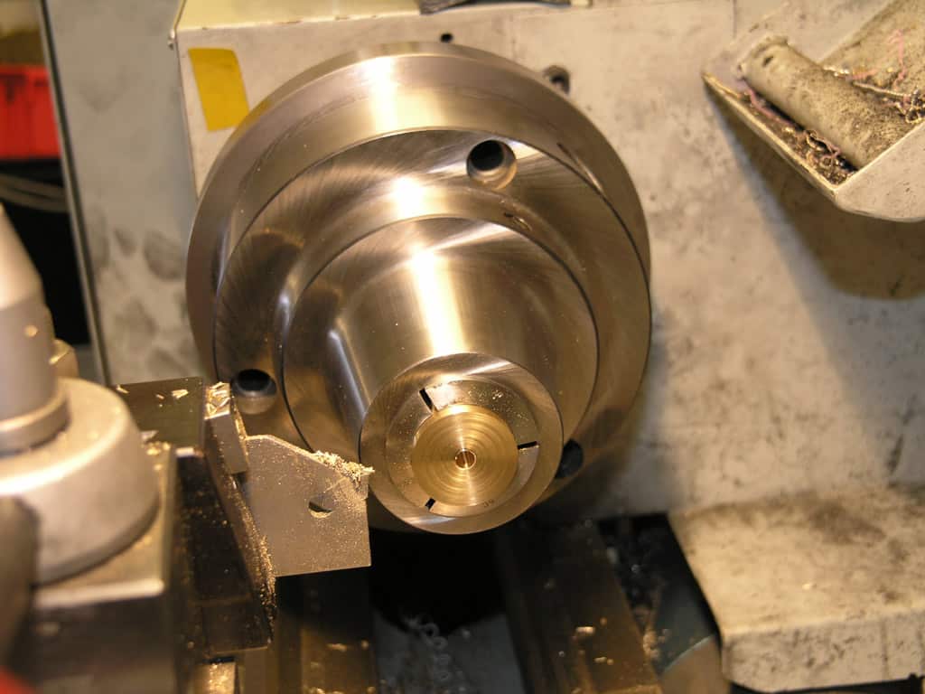 Metal lathe tool head with spindle and brass object on a cluttered work surface.