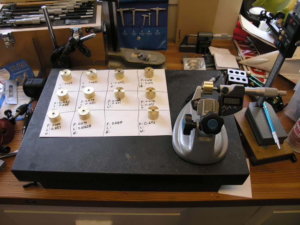 Cluttered workbench with tools, microscope, calipers and handwritten notes.