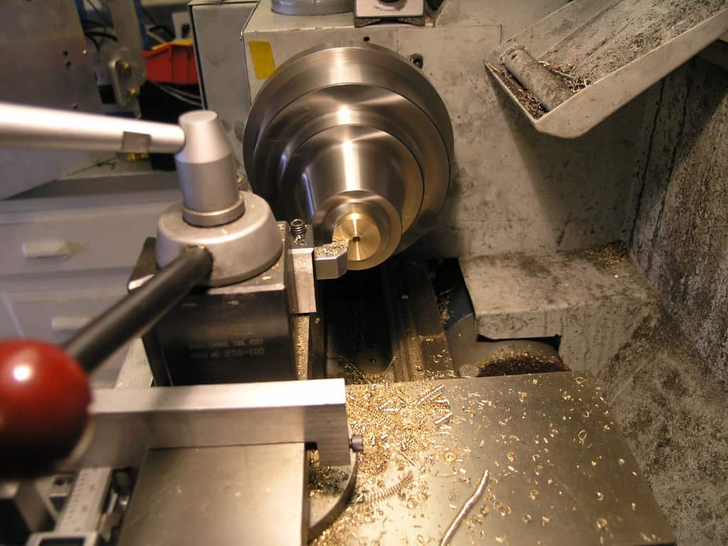 Lathe machine with tools and equipment surrounding a large metal component on a gray background.