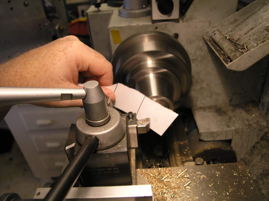A person operating a lathe in a workshop with surrounding tools and materials.