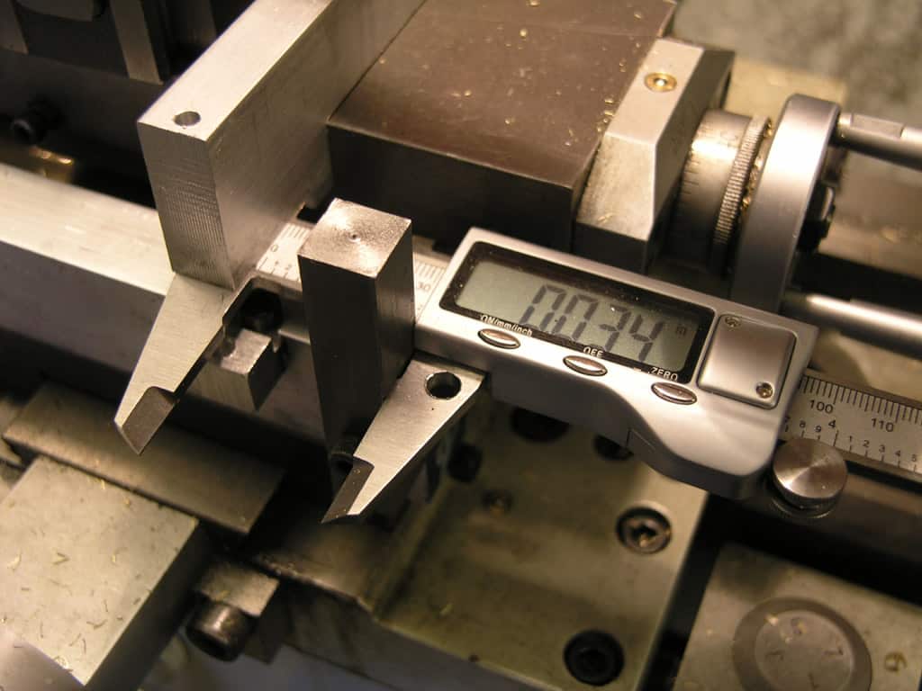 Digital caliper on metal workbench with various tools and machinery.