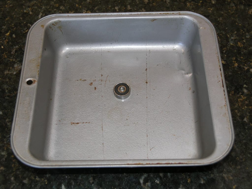 Silver-colored metal sink with single drain, stainless steel or aluminum construction, on black granite countertop.