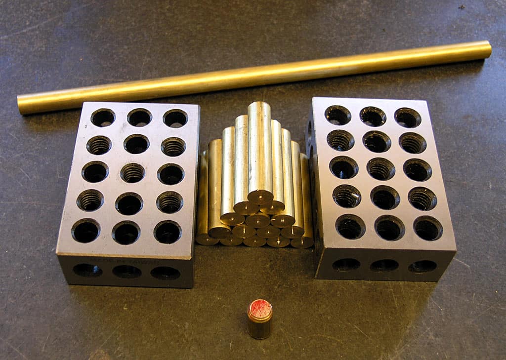 Brass rods and rectangular steel blocks with threaded holes on a dark background.
