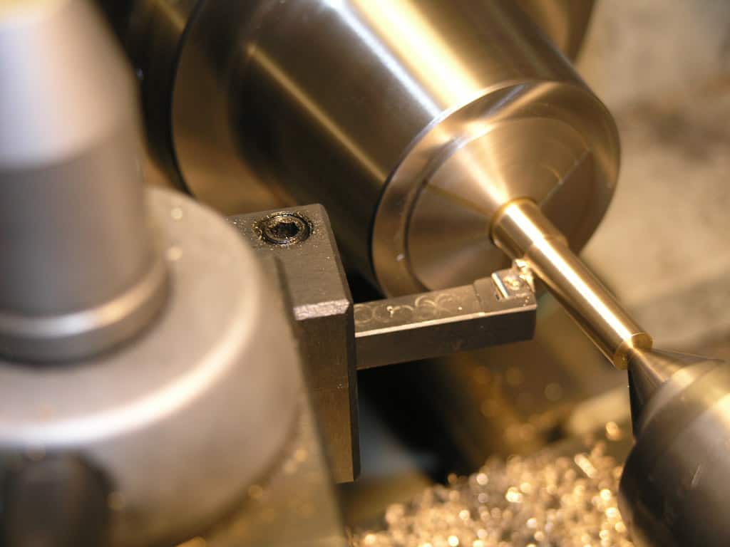Metal lathe with machined brass piece and surrounding tools.