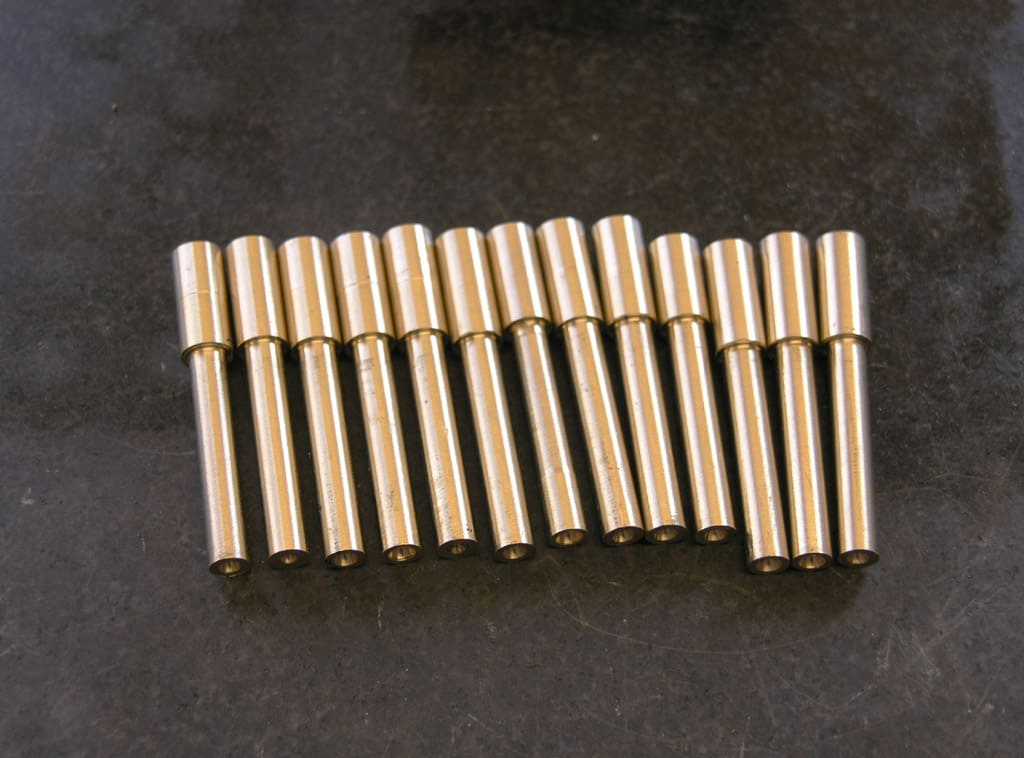 Brass dowel pins arranged in two rows on a dark gray surface.