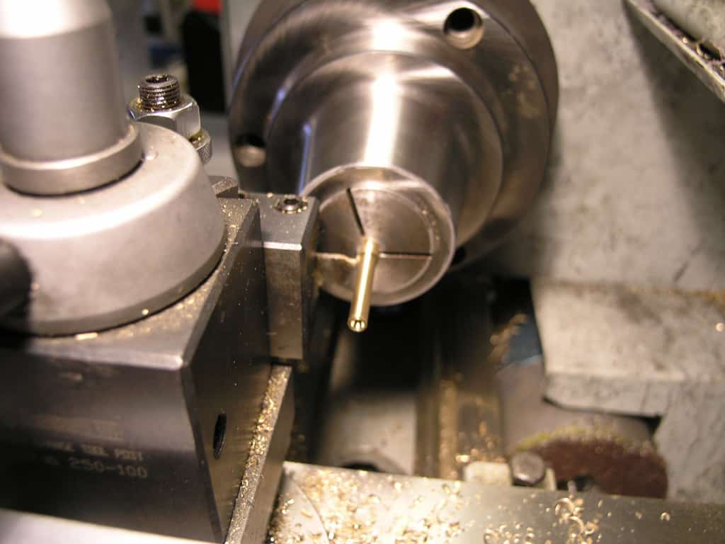 Metalwork on a lathe with threads, cutting tool, and shavings.