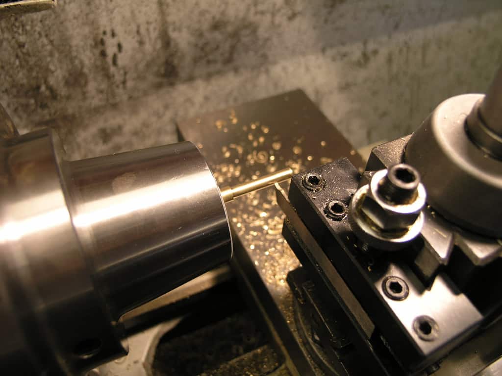 Lathe machine with cutting tool in action, spinning rapidly as it cuts brass rod.
