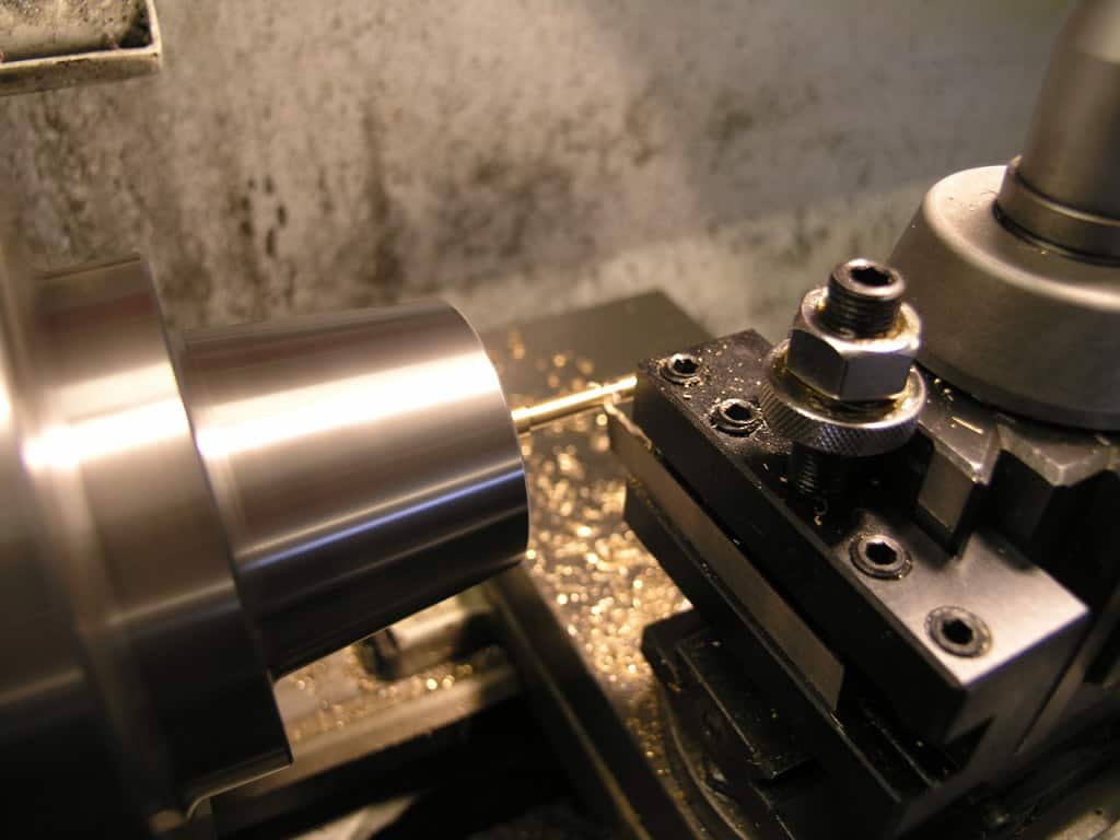 Metalworking lathe in use, spindle and tool post with end mill or drill bit visible.