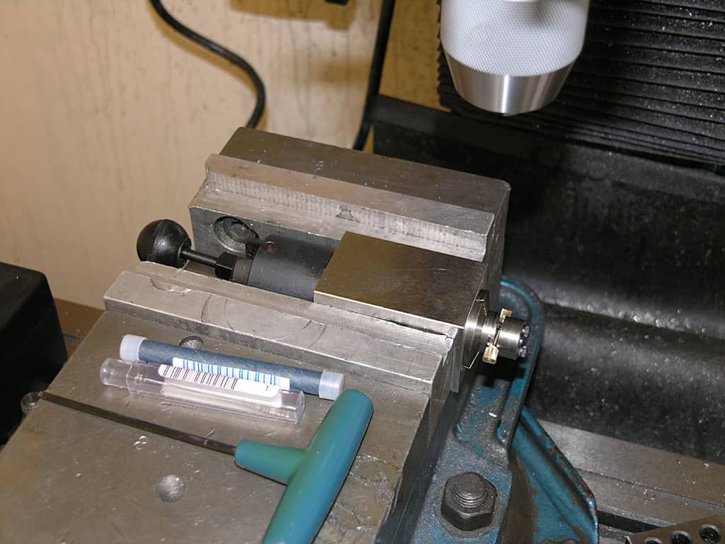 Metalworking vise with set screw, clamping tool, and ruler on a workshop workbench.