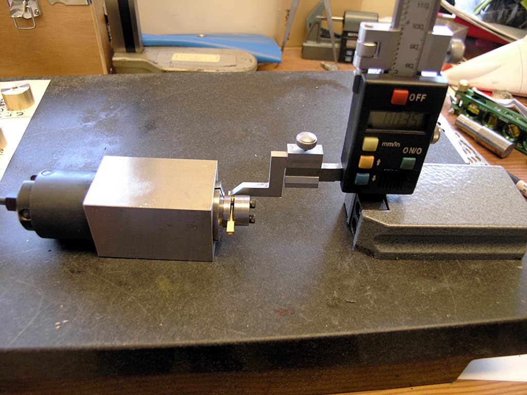 Digital caliper with black body and clear LCD display on cluttered workbench.