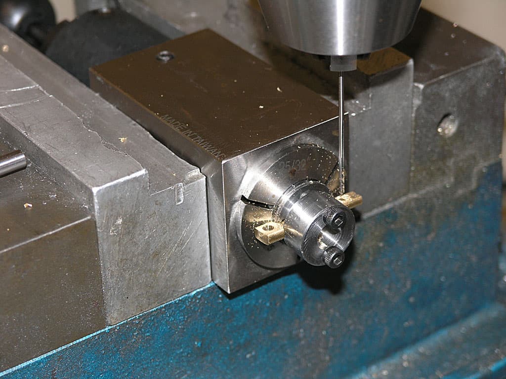 A metalworking machine with a drill bit attached to a metal rod, positioned on top of a workpiece.