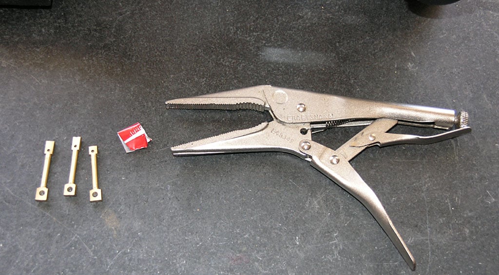 Silver pliers with serrated jaws, Craftsmen branding, small metal pieces with square holes nearby.