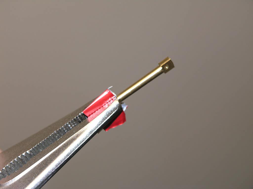 Metallic object with red tape measure attached, angled and partially hidden on a gray background.